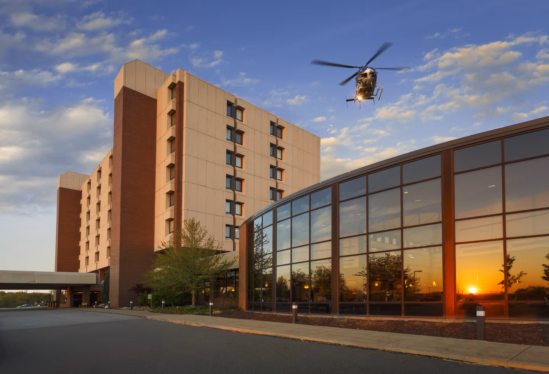 Exterior view of Weirton Medical Center main hospital with helicopter overhead at sunset.
