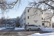 Snowy exterior view of Wildwood Manor senior living building with a parked car.