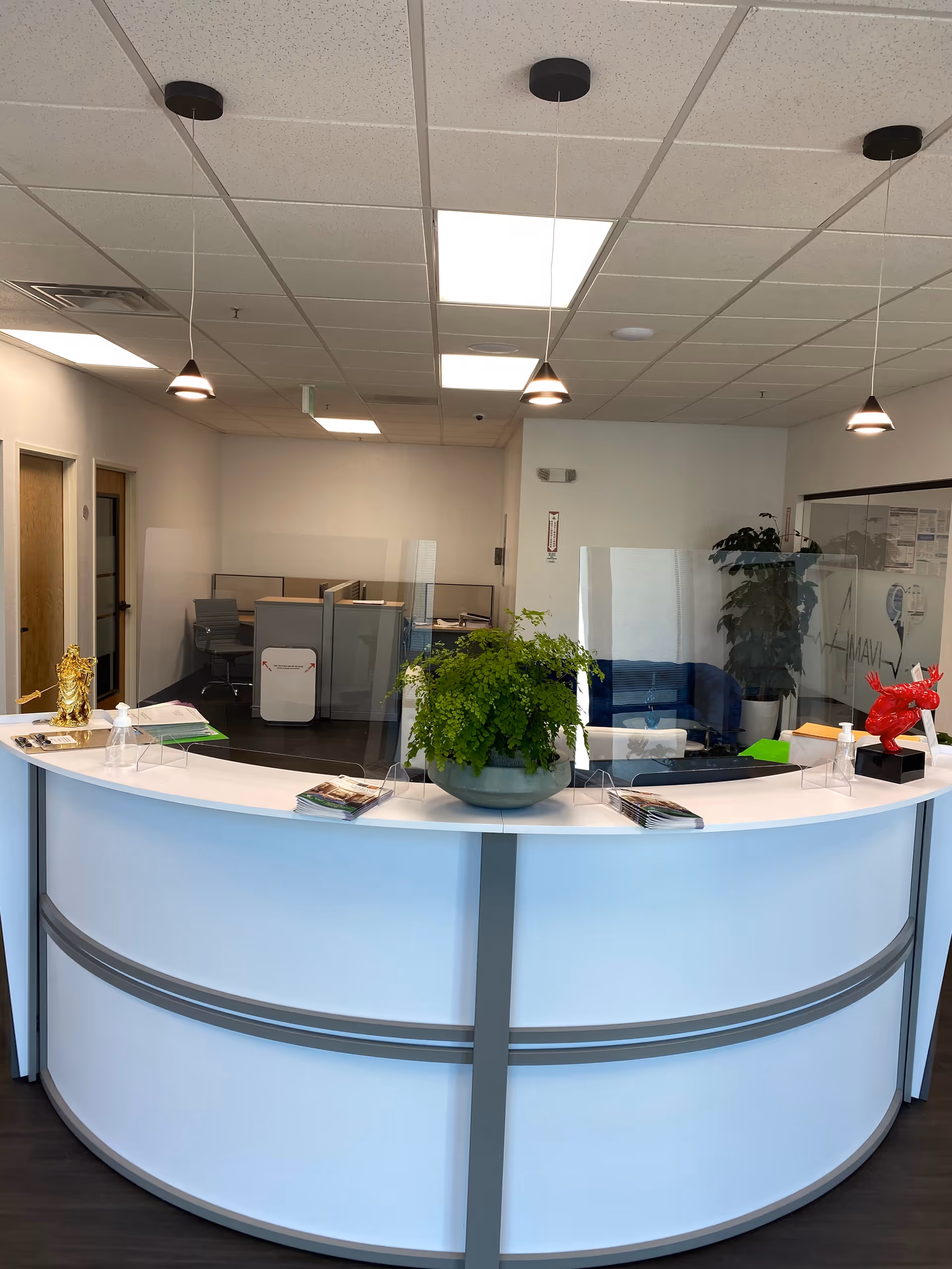 Modern reception desk arches in a bright, quiet lobby with plants and glass partitions.