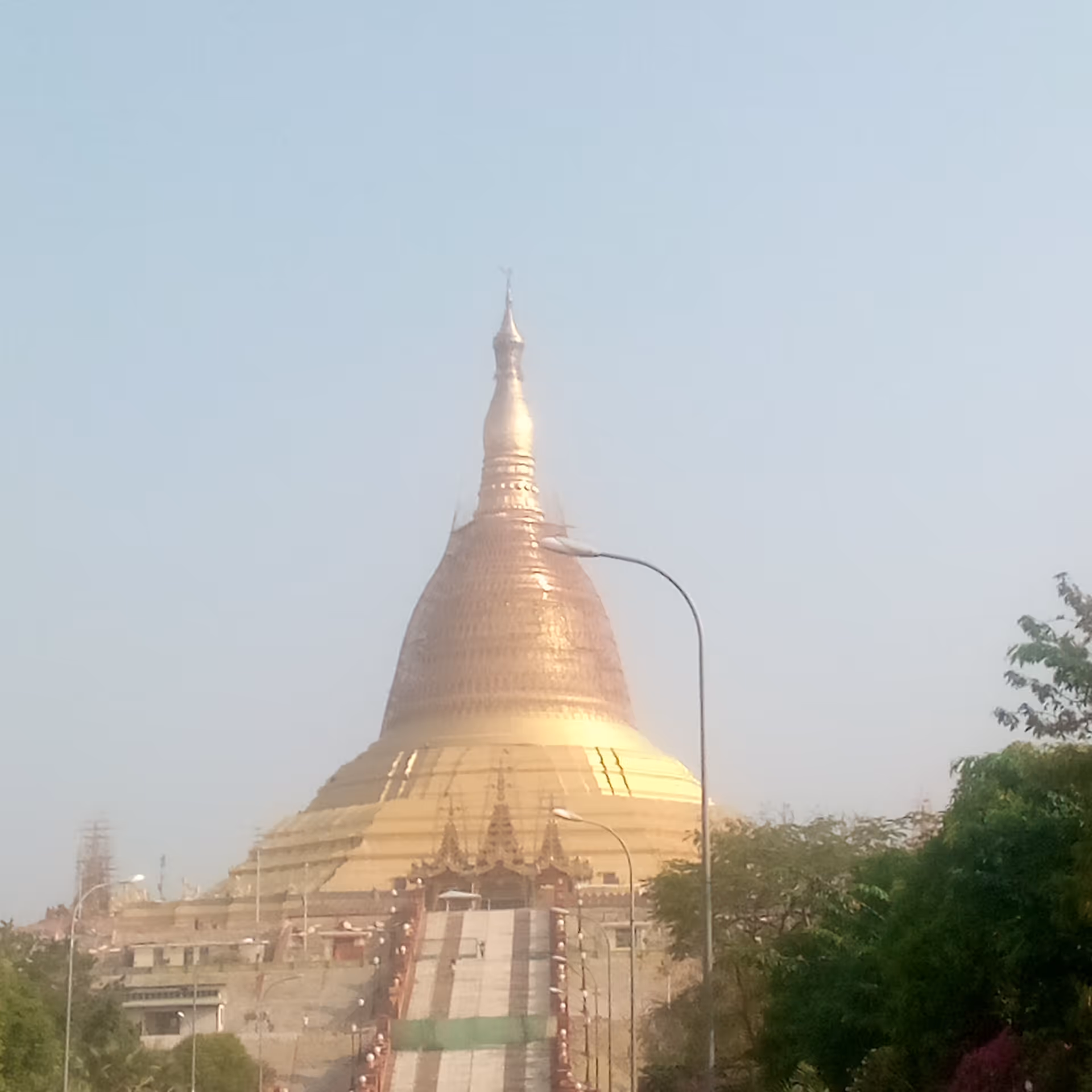 Golden pagoda with staircase, flanked by trees and street lamps under a clear sky.