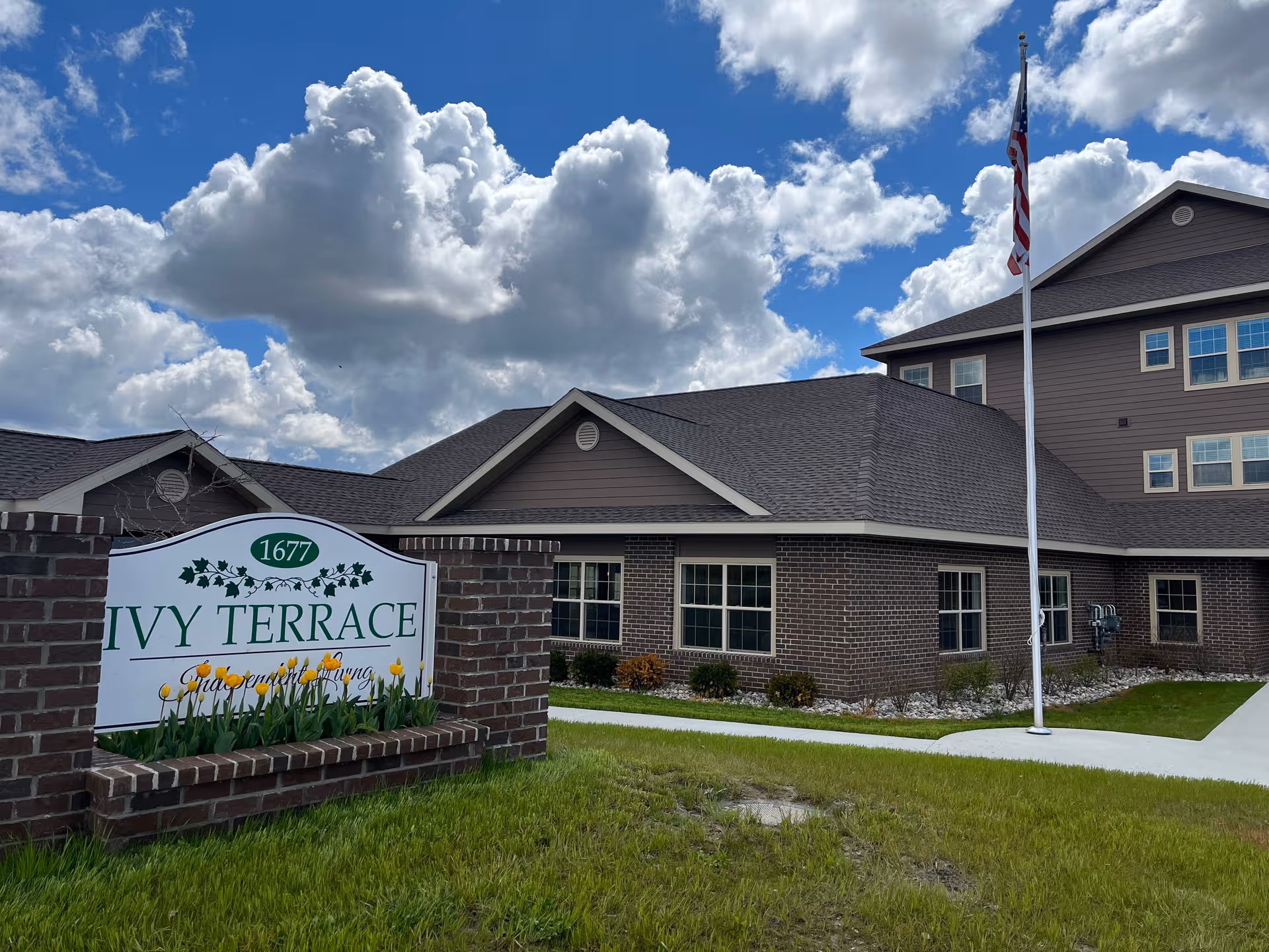 Outdoor view of Ivy Terrace senior living building with sign, brick facade, and flag.