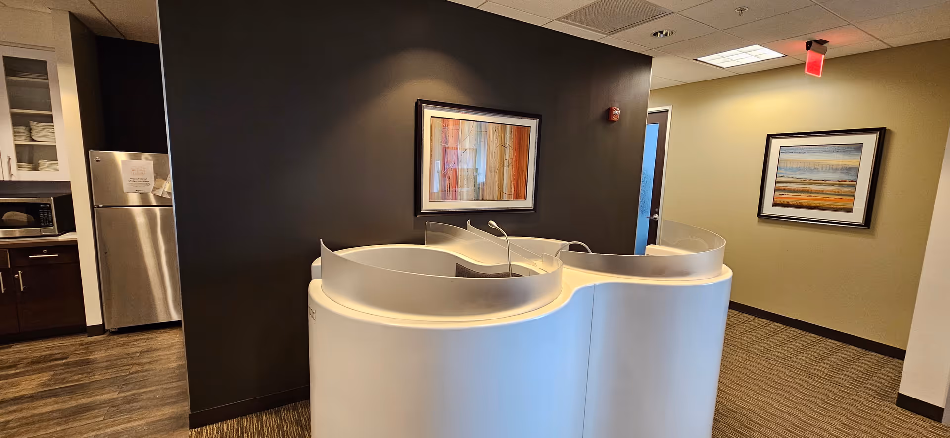 Curved white reception desk sits in a hallway with framed art on a dark wall.