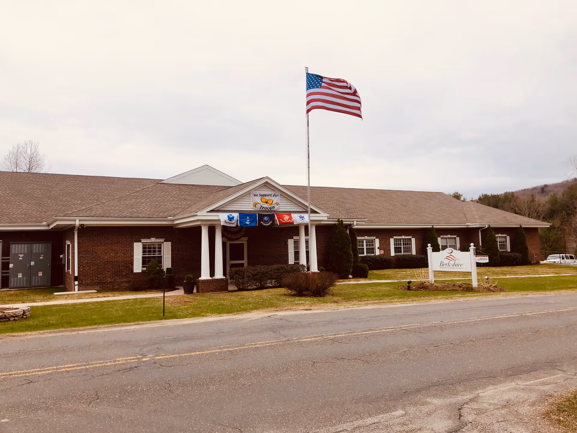 Single story brick senior living facility with American flag, entrance columns, and Berkshire sign.