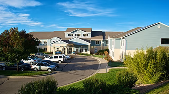 Exterior view of The Fountains of Hilltop senior living facility with a curved driveway and parking