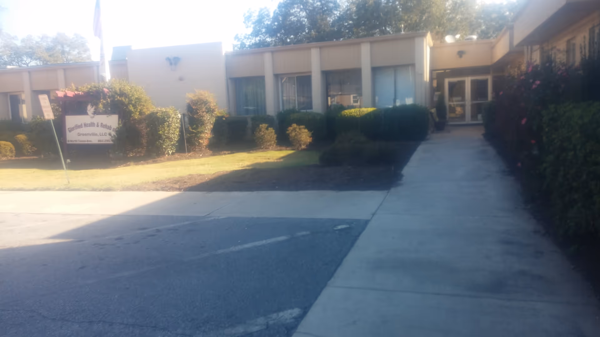 Exterior view of a single-story senior living facility entrance with shrubs and a sidewalk.