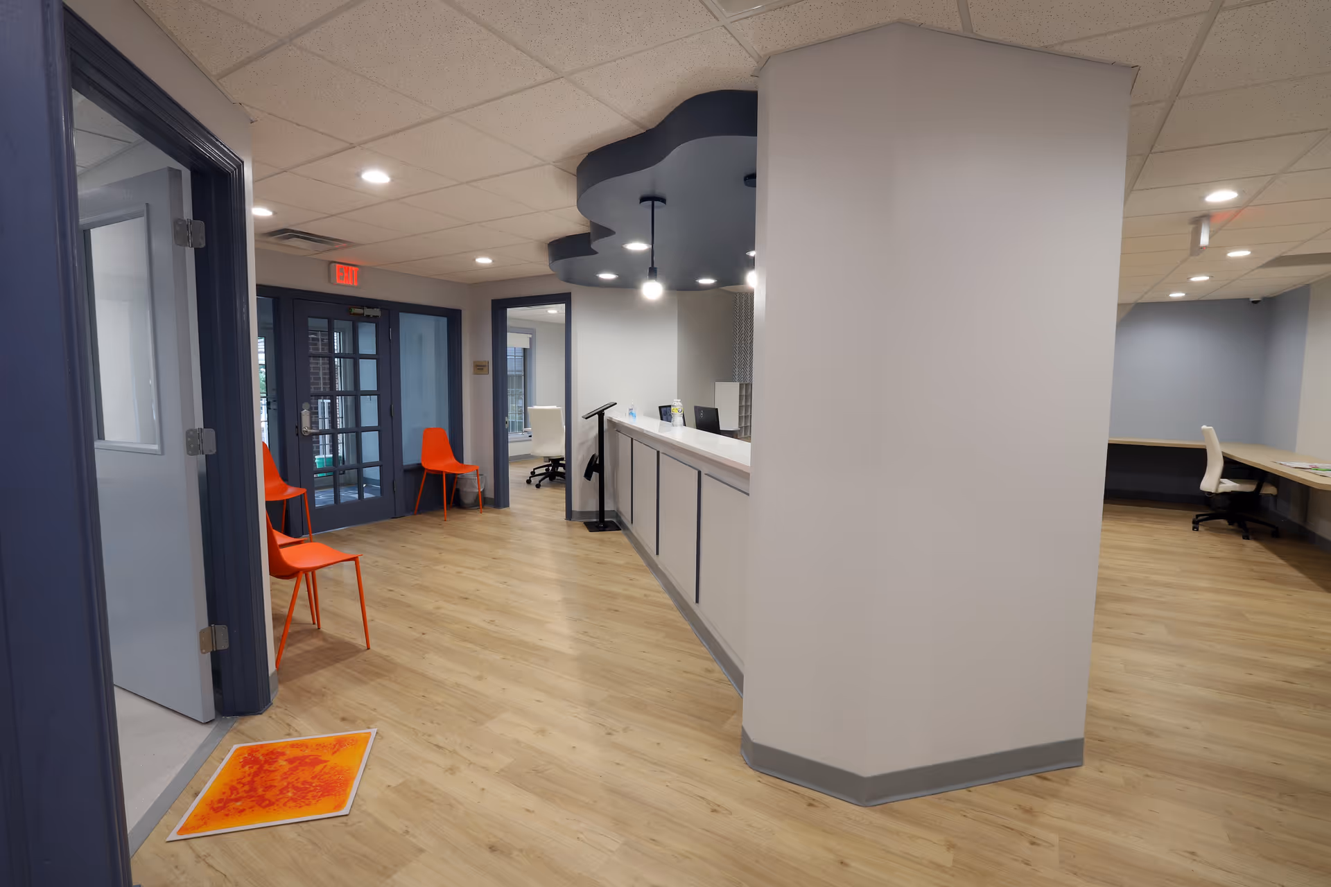 Empty modern reception area with a long counter, orange chairs, and wood flooring.