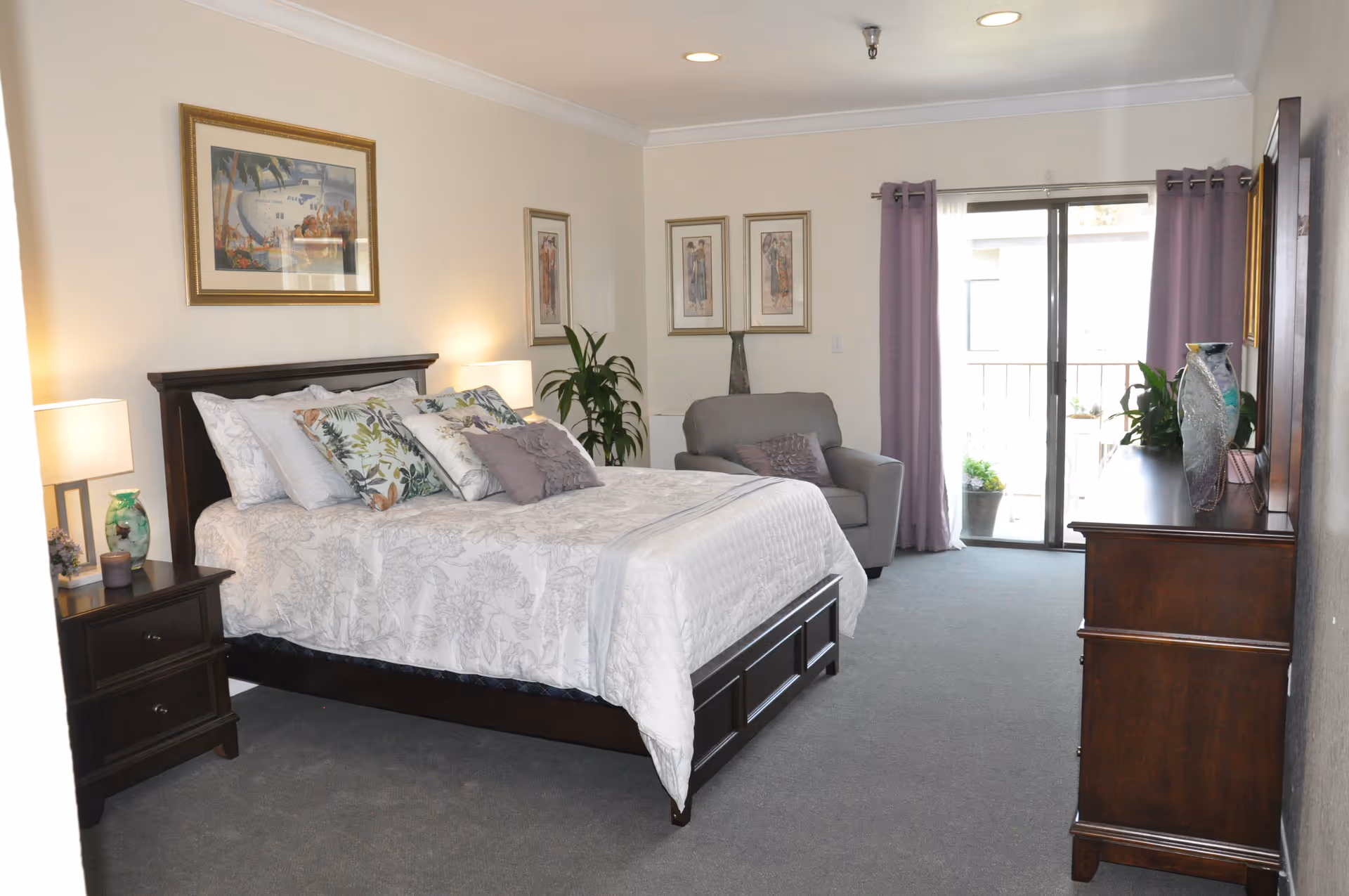 A spacious bedroom with a large bed, nightstands, a dresser, and glass doors to a balcony.