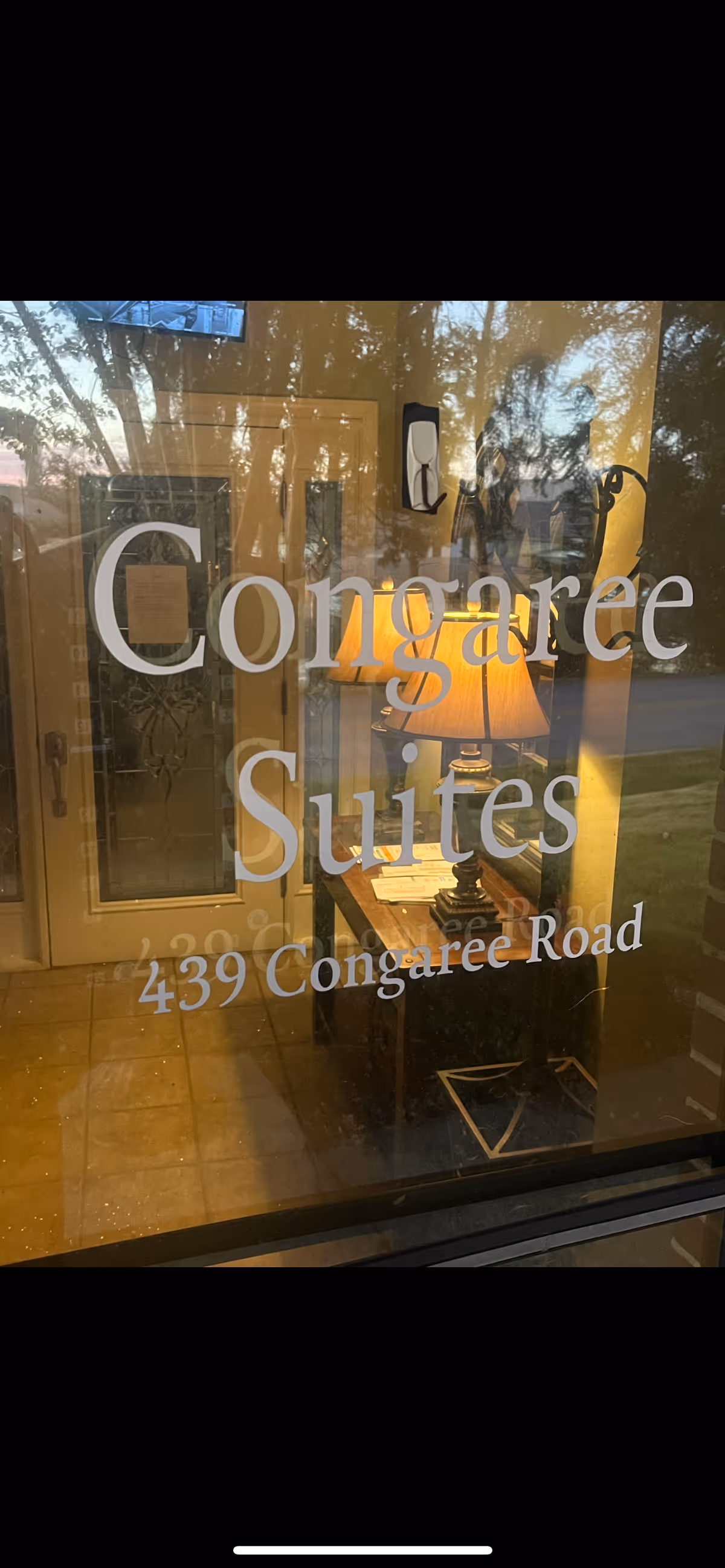 Through glass window, interior lobby with lamp and Congaree Suites signage.