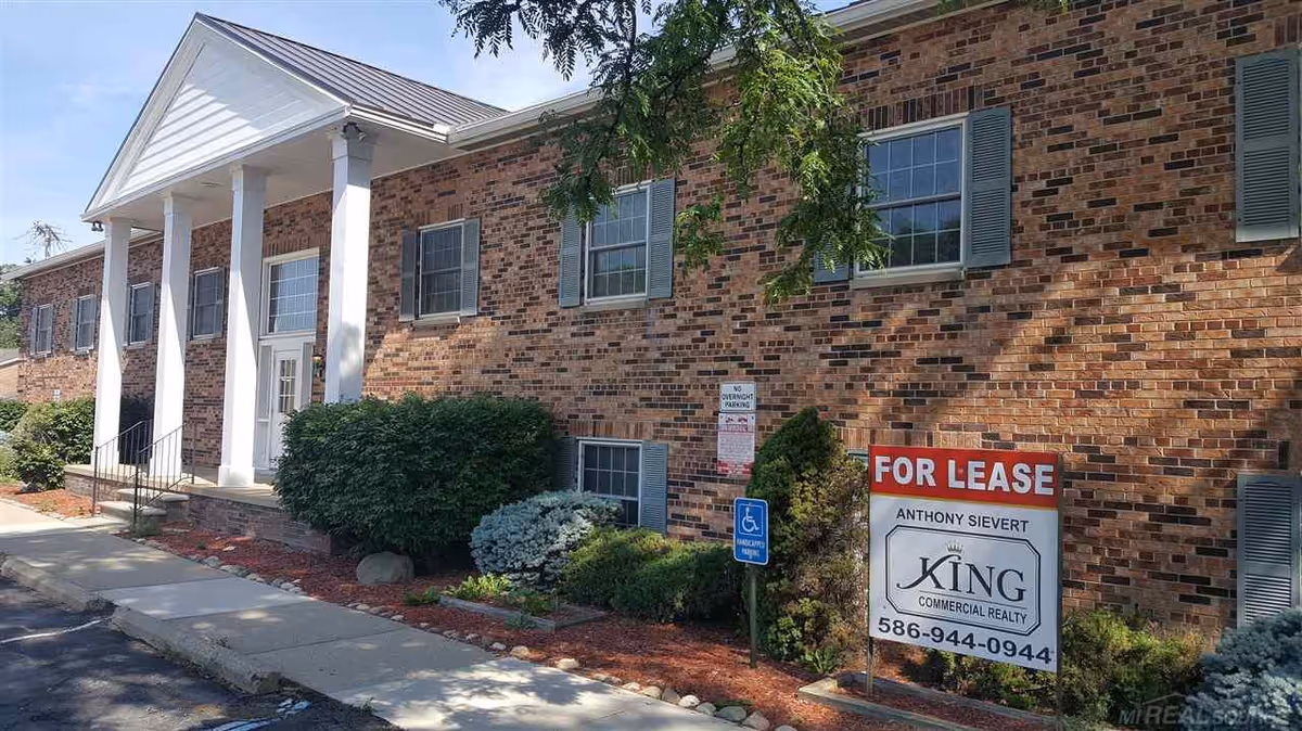 Brick senior living facility exterior with a covered front entrance and a for-lease sign.