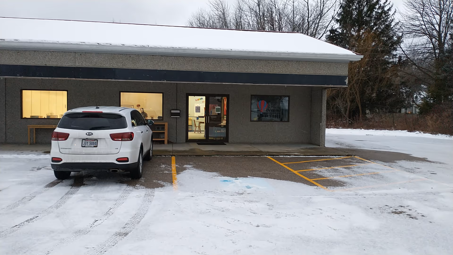 Exterior view of a single-story building with a white SUV parked in a snowy lot.