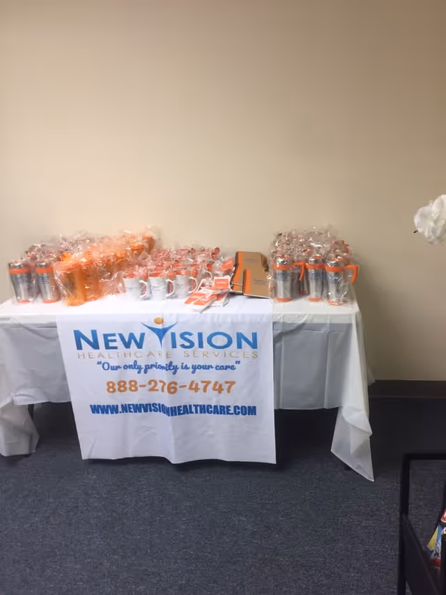 Table displays New Vision Healthcare Services banner with wrapped cups and promotional materials.