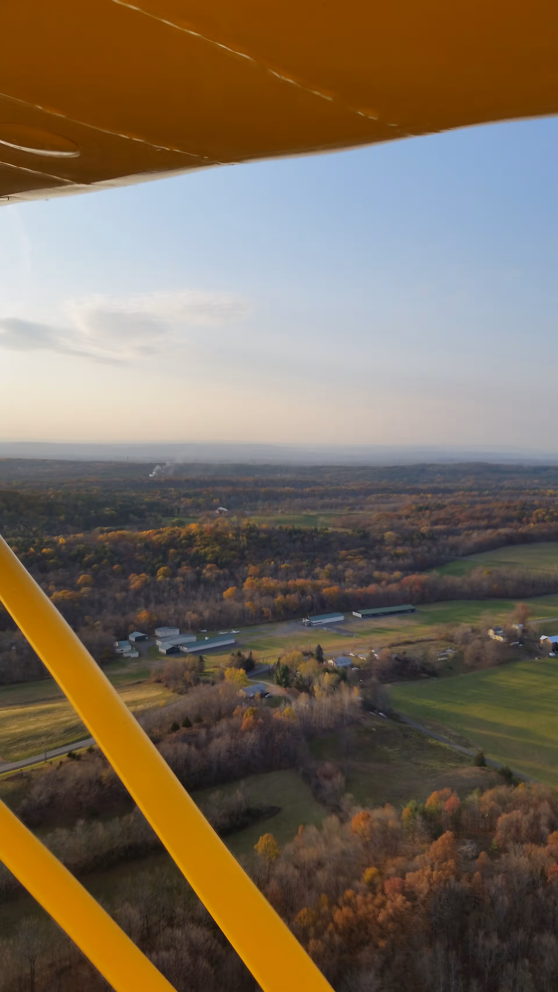 Aerial view of rural landscape with trees and fields, yellow aircraft wing in frame.