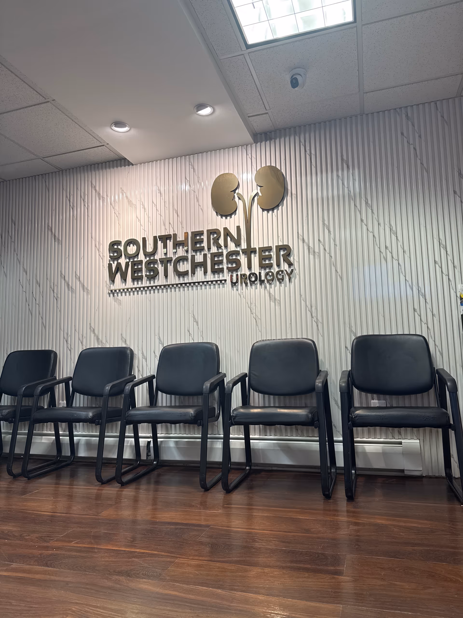 Interior waiting area with rows of black chairs and a Southern Westchester Urology sign.