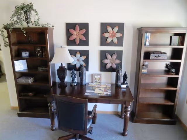 Wooden desk with chair, two tall bookcases, and four flower-art panels on the wall.