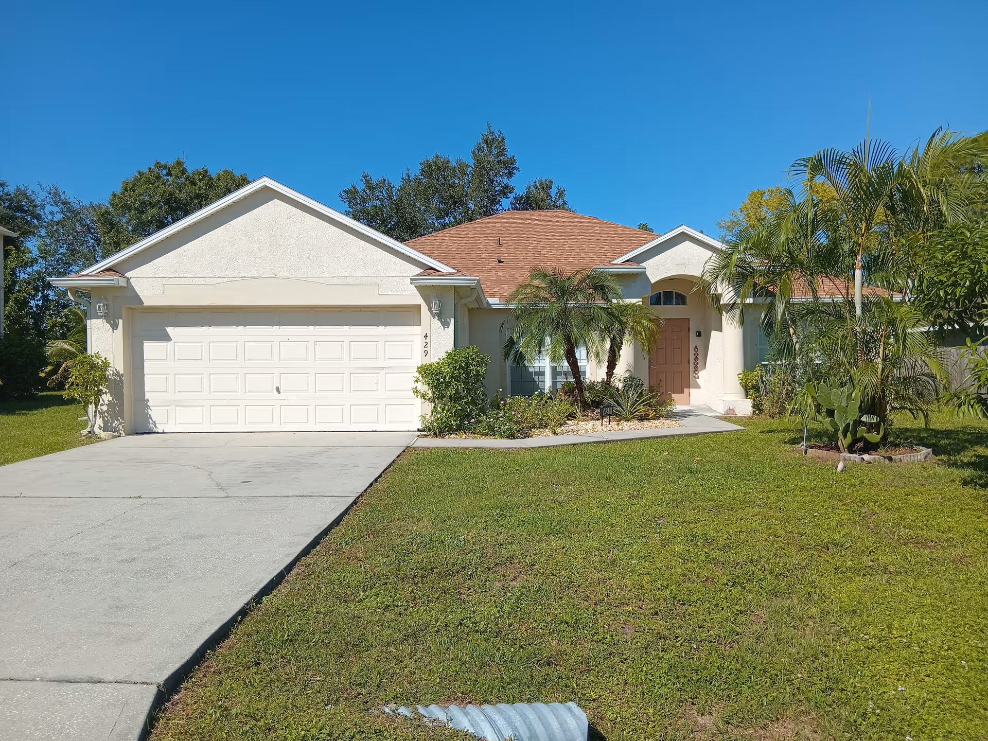 A single-story house with a two-car garage, palm trees, and a well-kept front lawn.