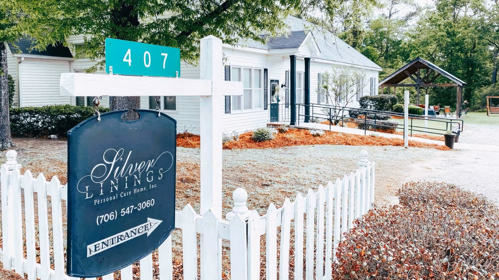 White single-story personal care home with a front yard picket fence and a large 'Silver Linings' sign displaying the address 407.