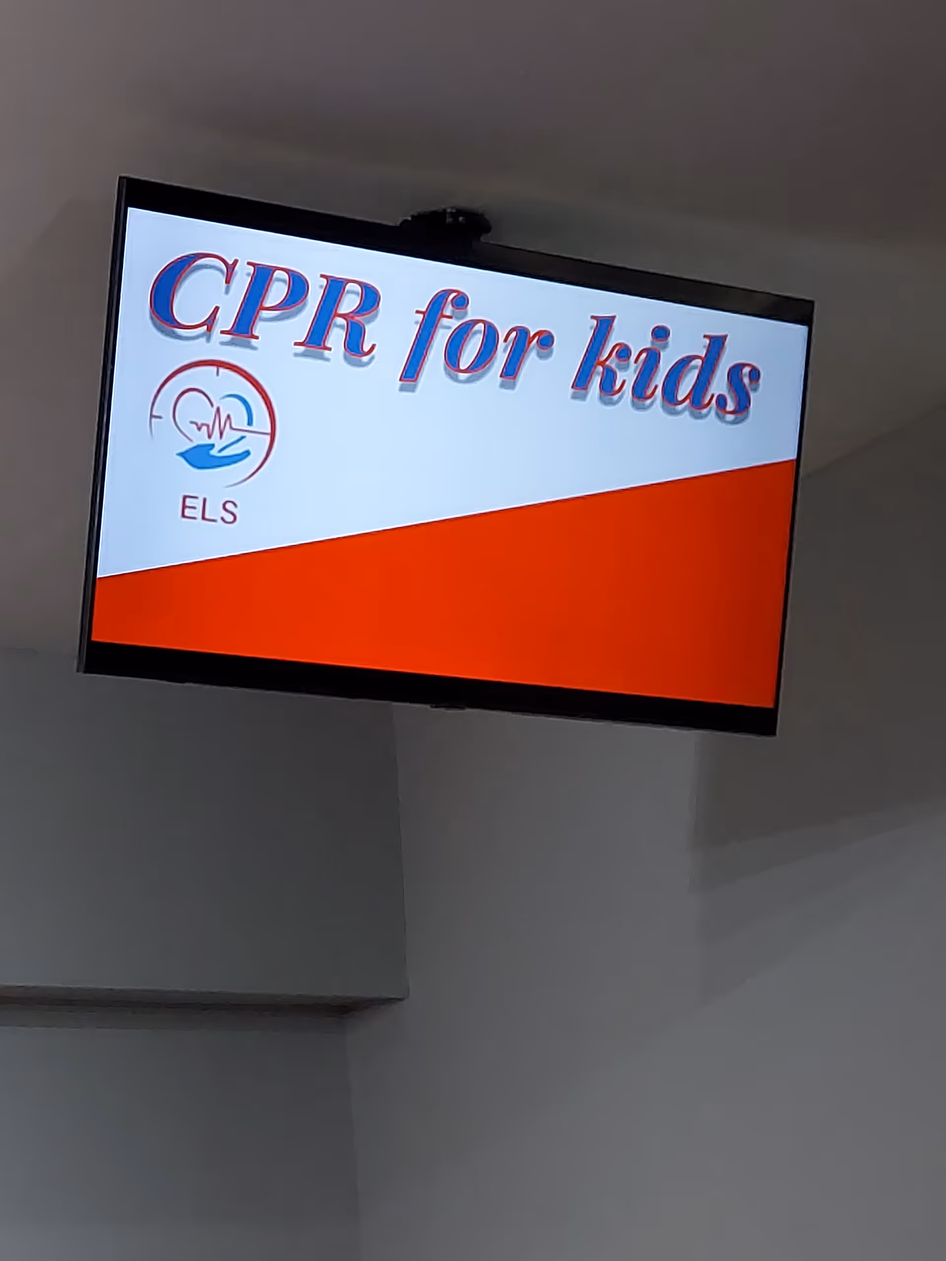 Mounted screen shows CPR for kids sign with ELS logo inside a facility.