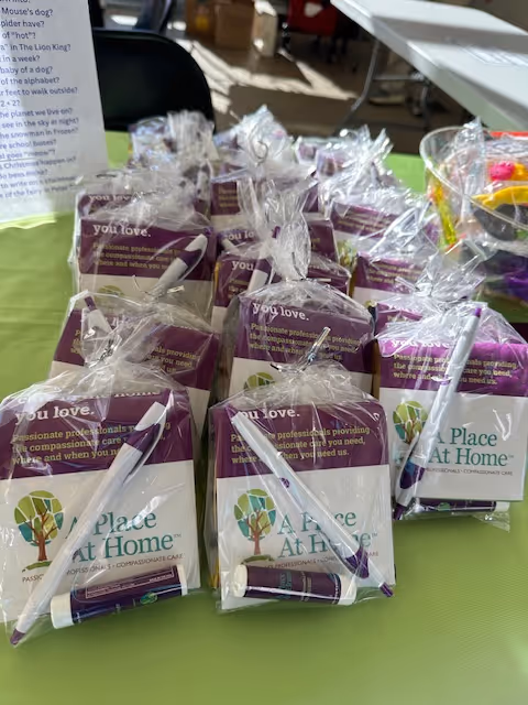 Row of purple-labeled A Place At Home gift packages with pens on a green table indoors