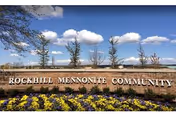 Stone sign reading Rockhill Mennonite Community with flowerbeds and blue sky.