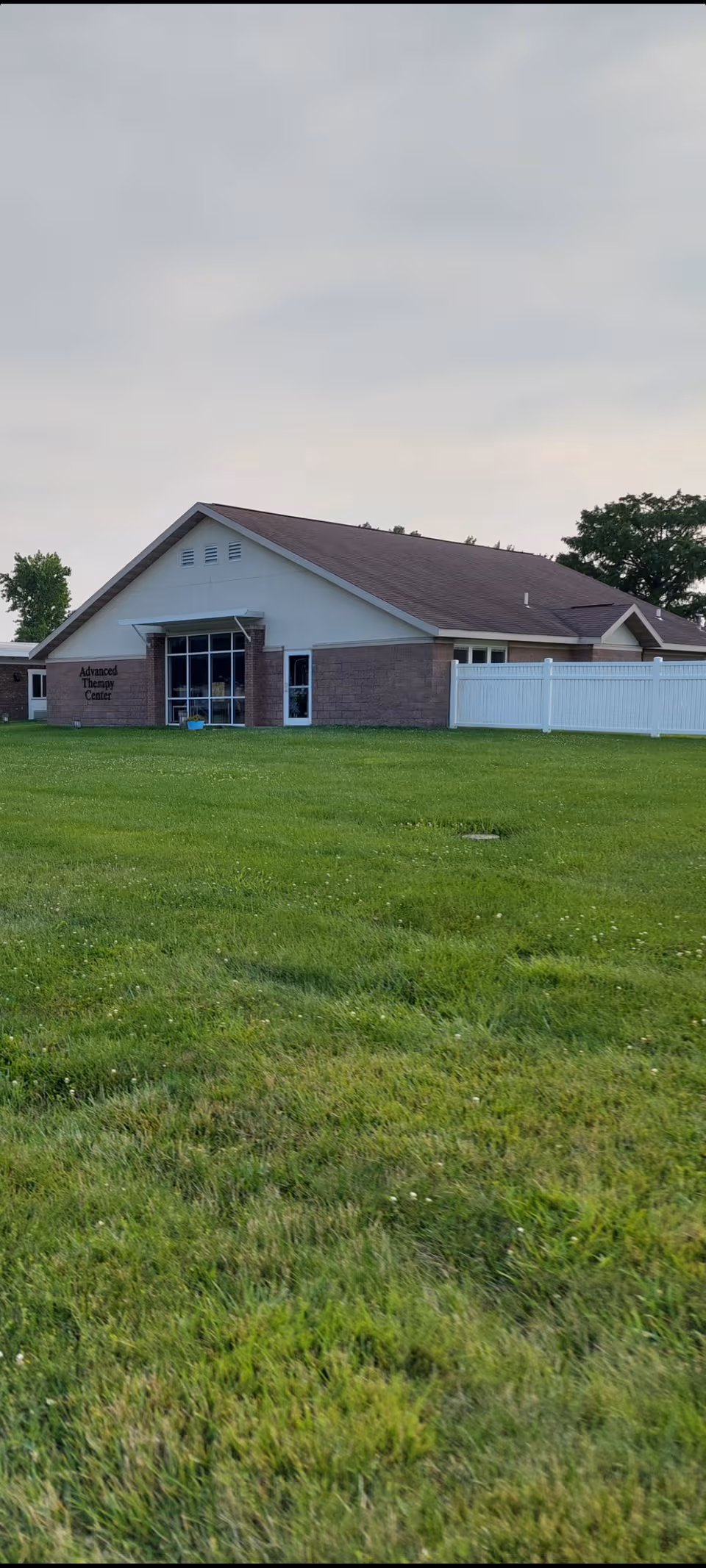 Single-story facility with brick accents sits on a grassy lawn under a cloudy sky.