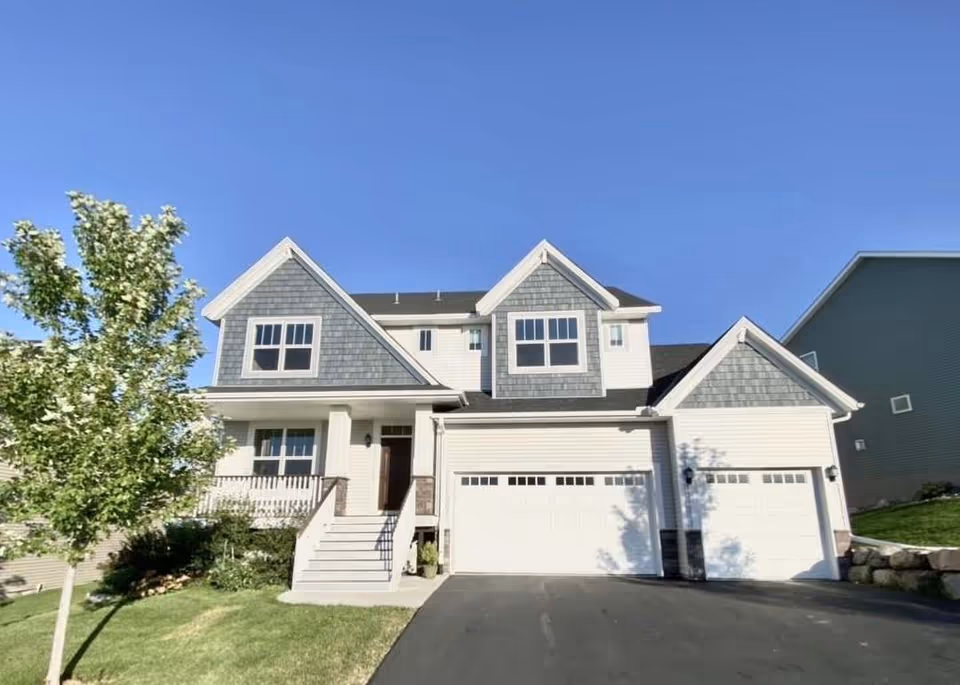 Two-story care facility exterior with a wide driveway, front steps, and blue sky.