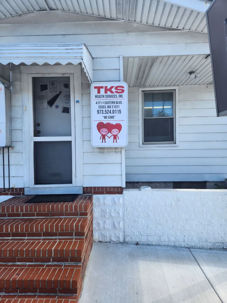 Exterior entrance to TKS Health Services building with steps, white siding, and a sign.