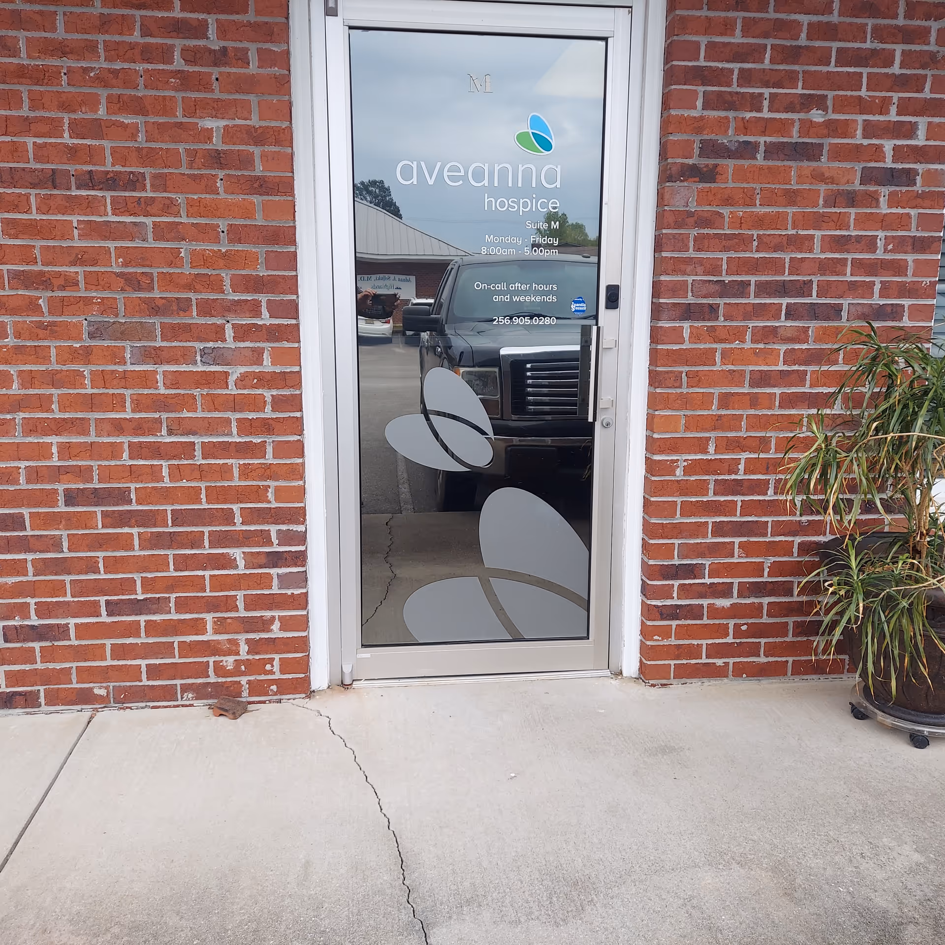 Glass door with Aveanna Hospice logo, brick wall, and potted plant outside.