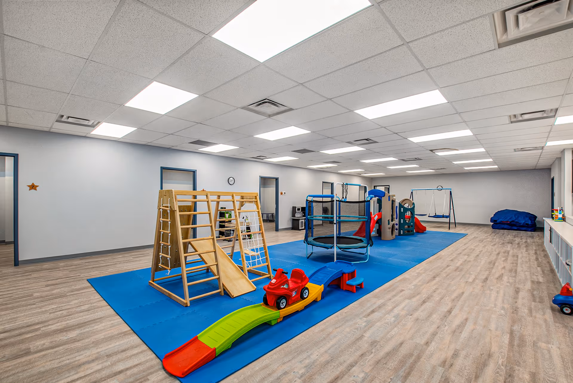 Indoor children's play area with gym equipment, blue mats, and wooden climbing frame.