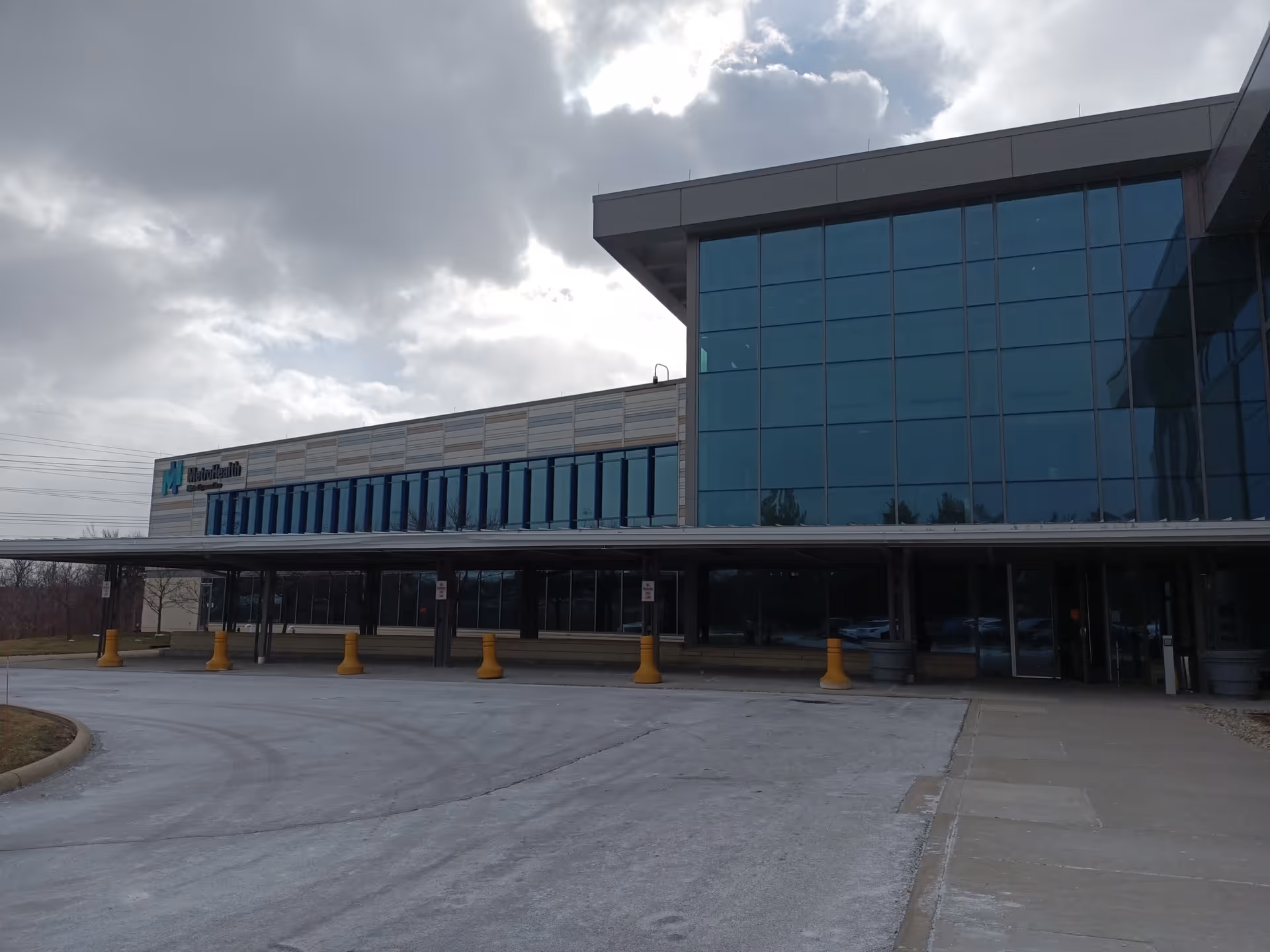 MetroHealth exterior with glass facade and covered entrance under cloudy sky.