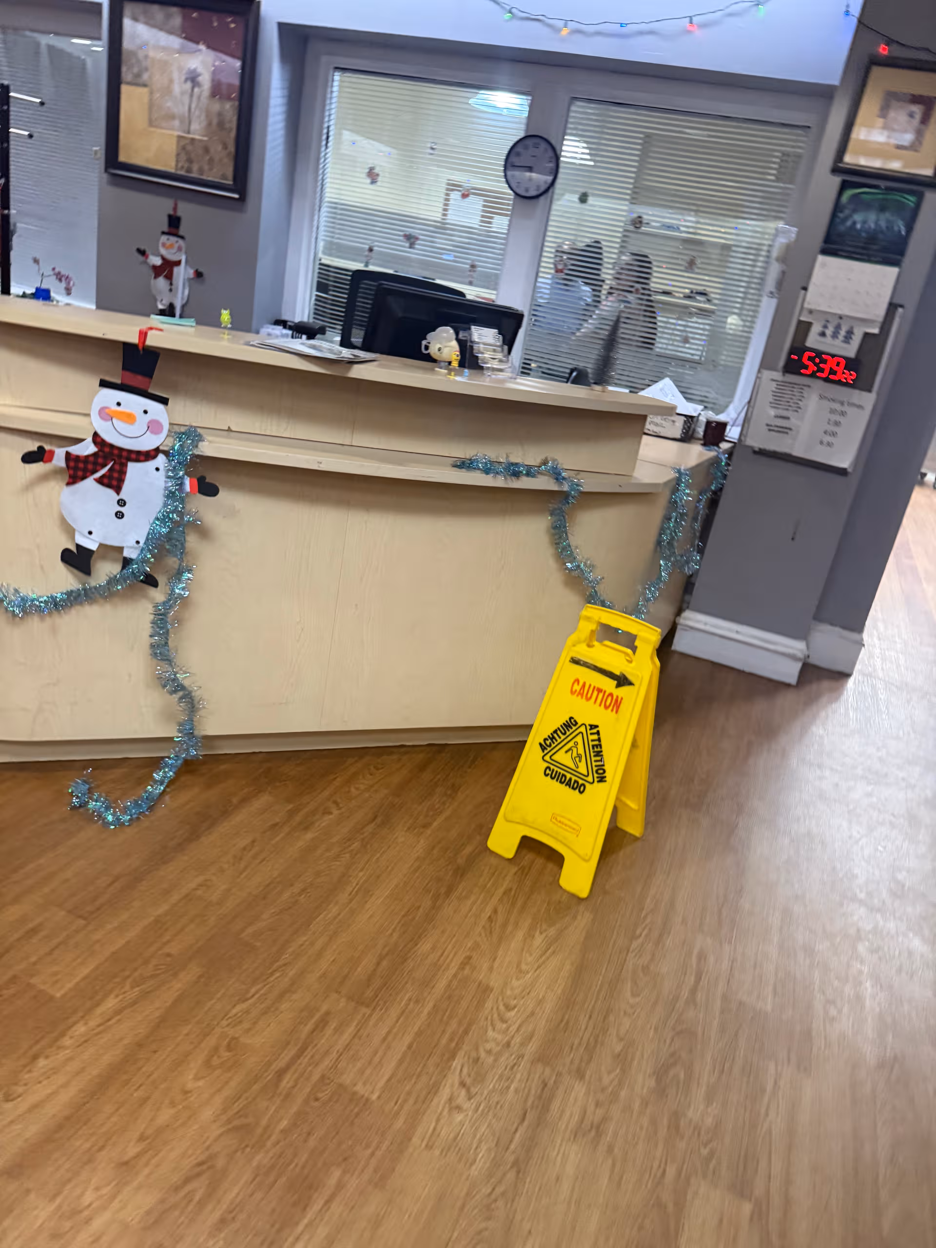 Front desk in a decorated senior center lobby with snowman garlands and a wet floor sign.
