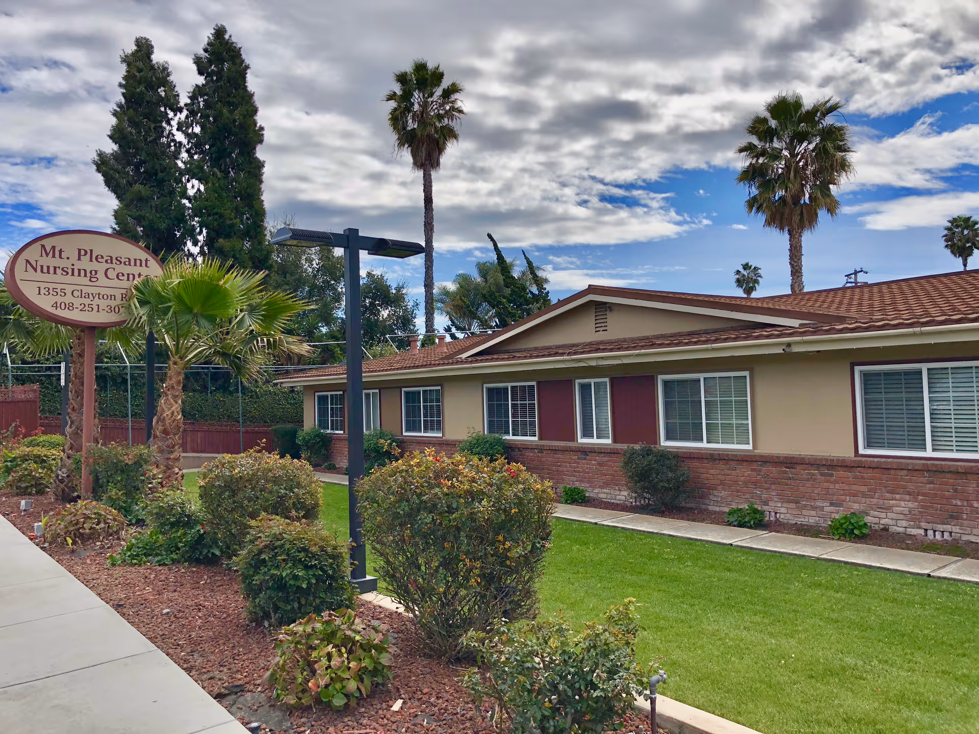 Single-story nursing center exterior with sign, landscaping, and palm trees along a sidewalk.
