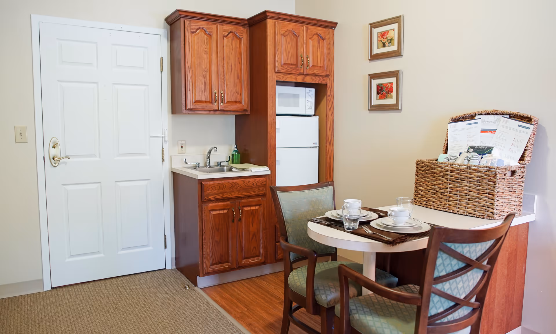 Small dining table with place settings beside a compact kitchen and wooden cabinets.