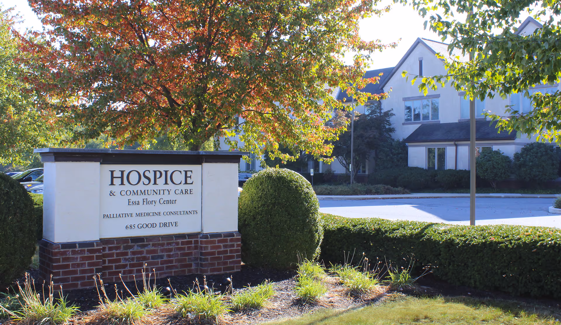 Exterior view of a Hospice & Community Care sign with a building in the background.