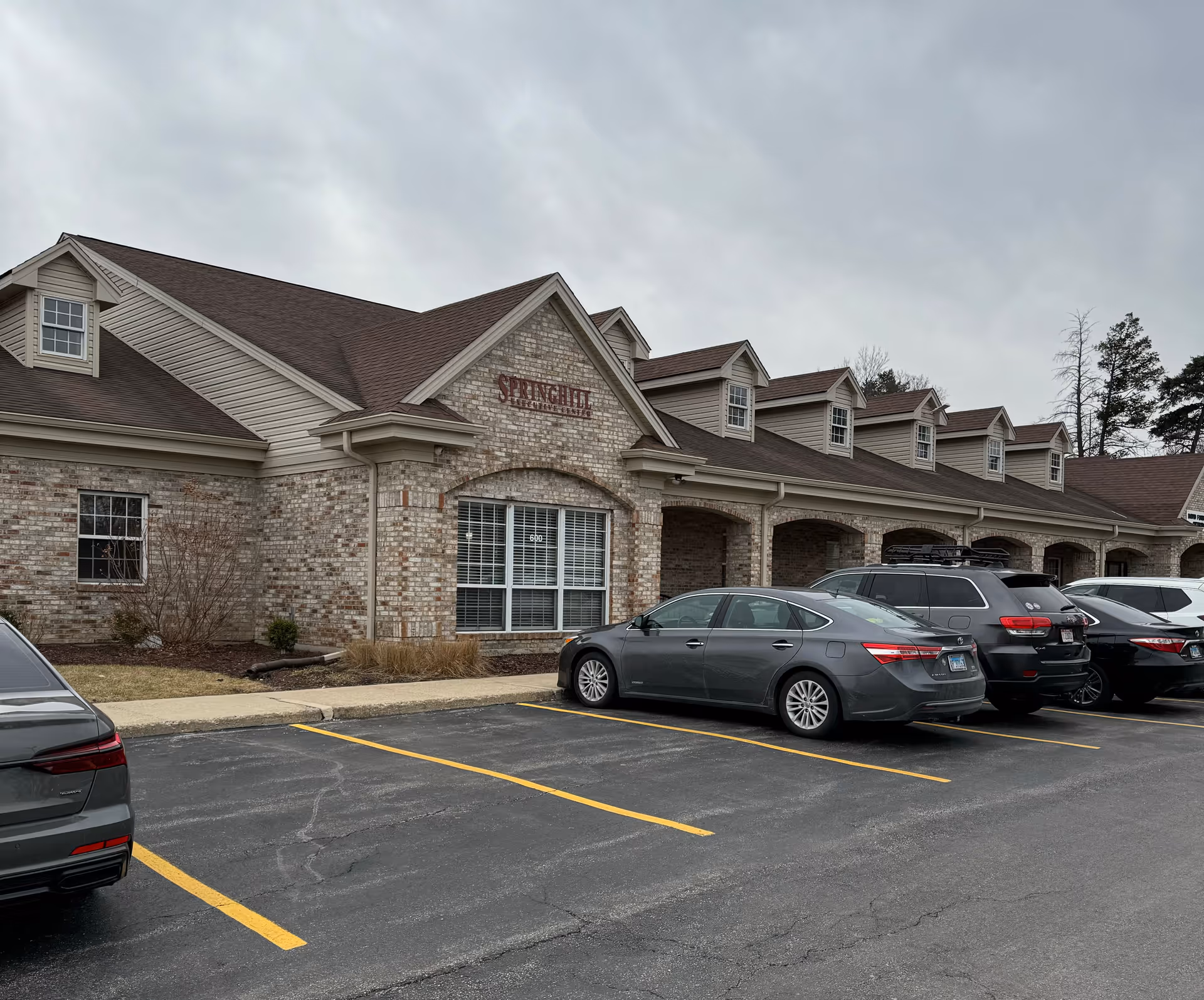 Exterior view of a senior living facility with brick facade and parked cars.