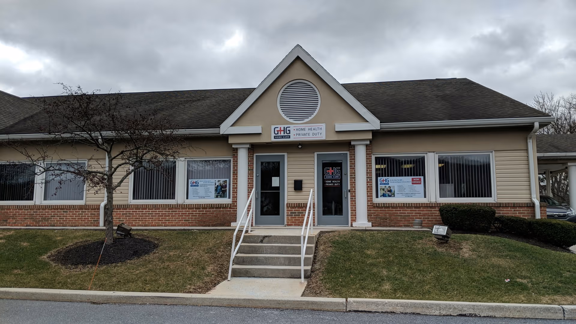 Front view of a single-story beige healthcare building with a peaked entrance and brick base.