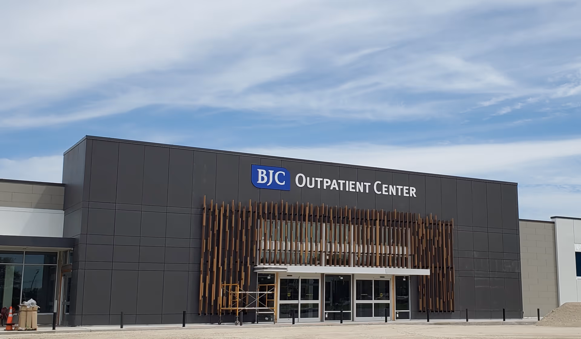 Modern outpatient center building with glass doors and wooden vertical slat facade.