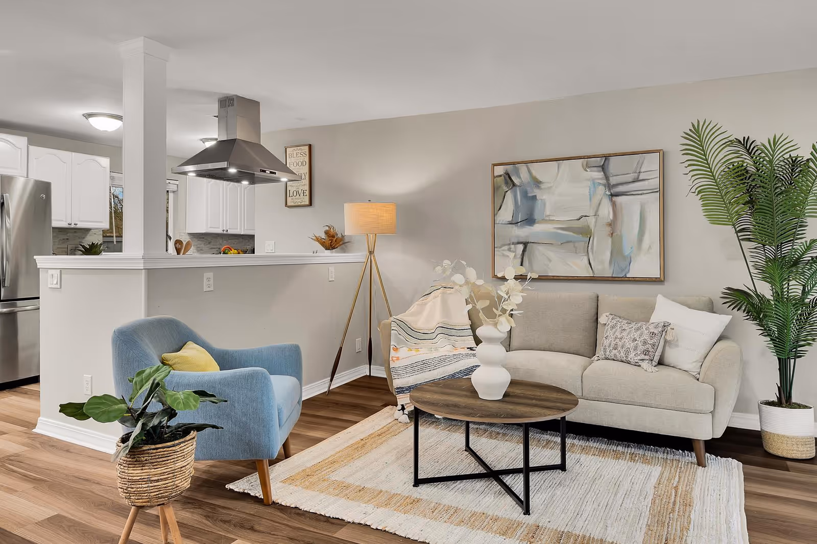 Bright modern living room with sofa, blue chair, coffee table, plant, and kitchen in background.