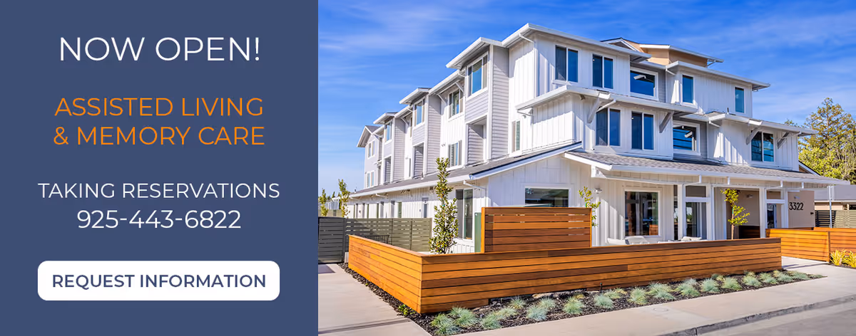 Modern senior living facility exterior with white siding and wooden privacy fencing.