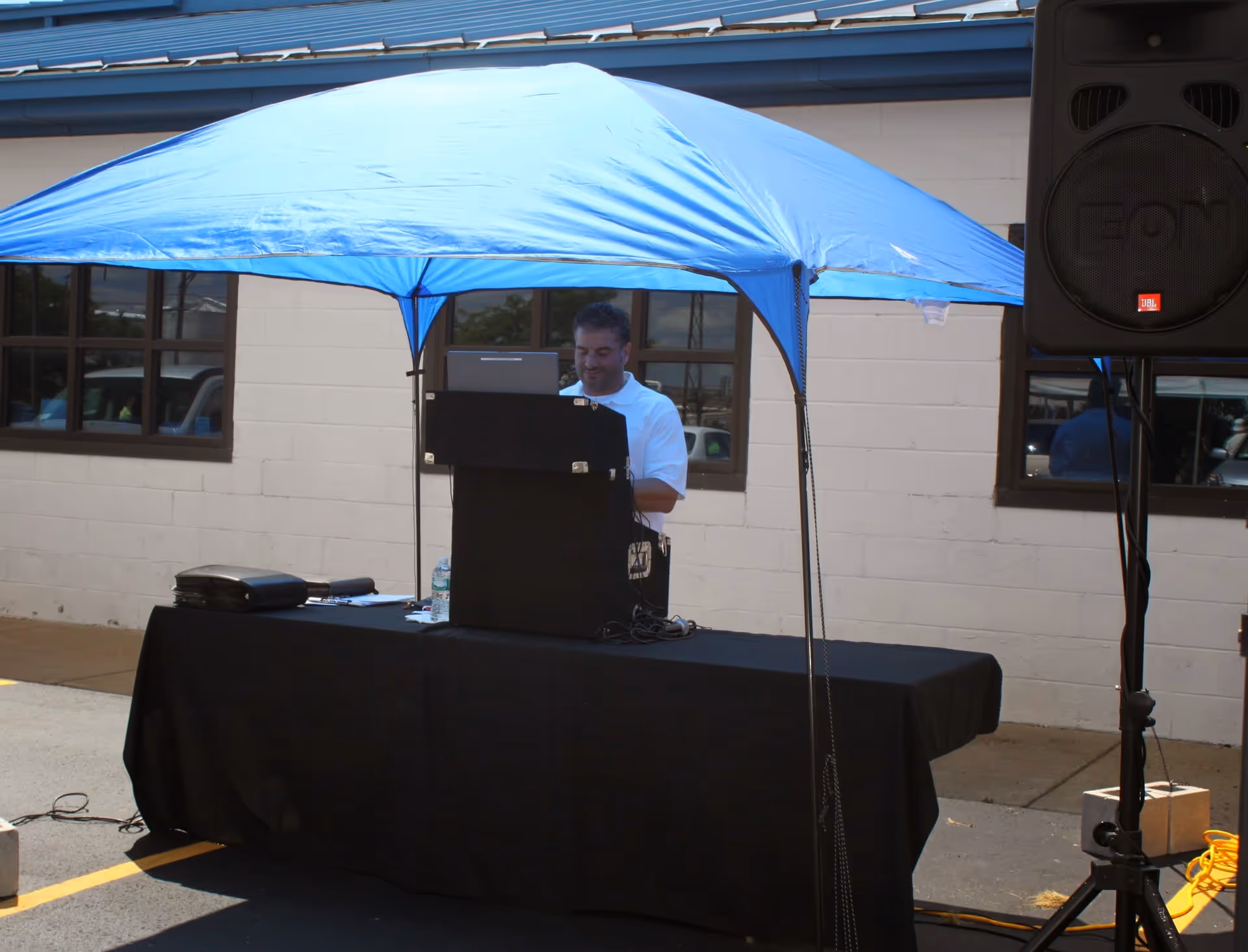 DJ booth under a blue canopy outdoors beside a building with a large speaker