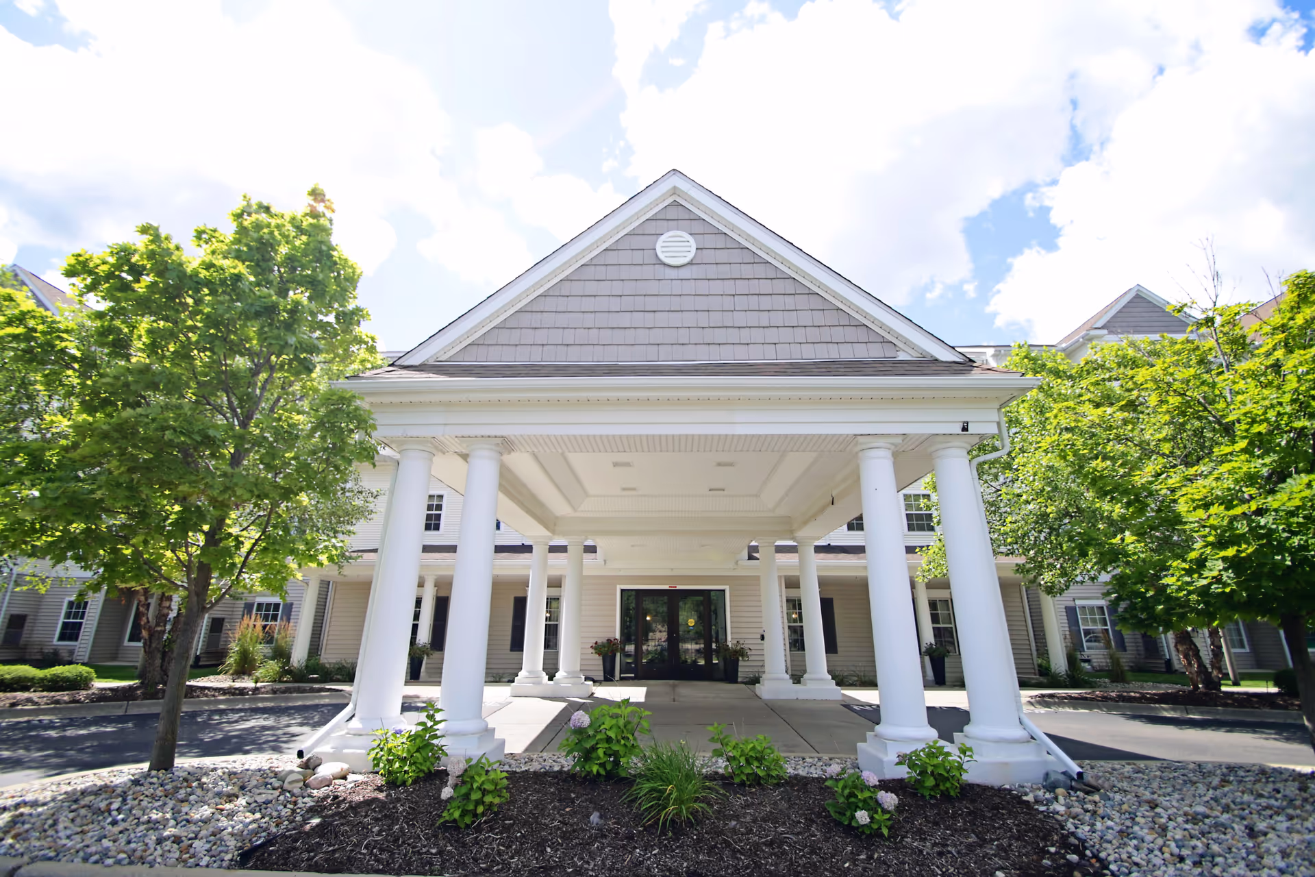 Front entrance of a senior living facility with white columns and a porte-cochere.