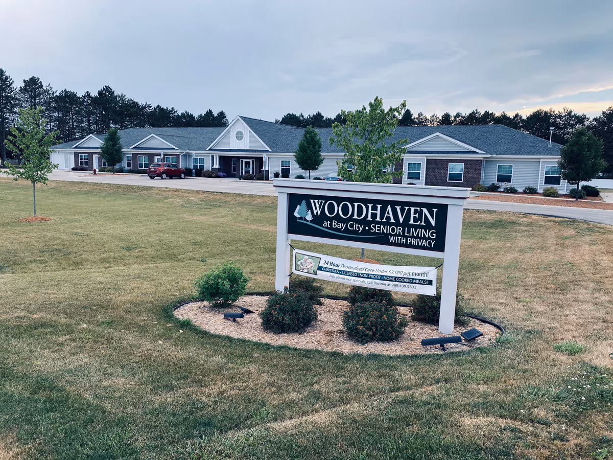Front lawn and sign reading 'Woodhaven at Bay City Senior Living' with the facility building in the background.