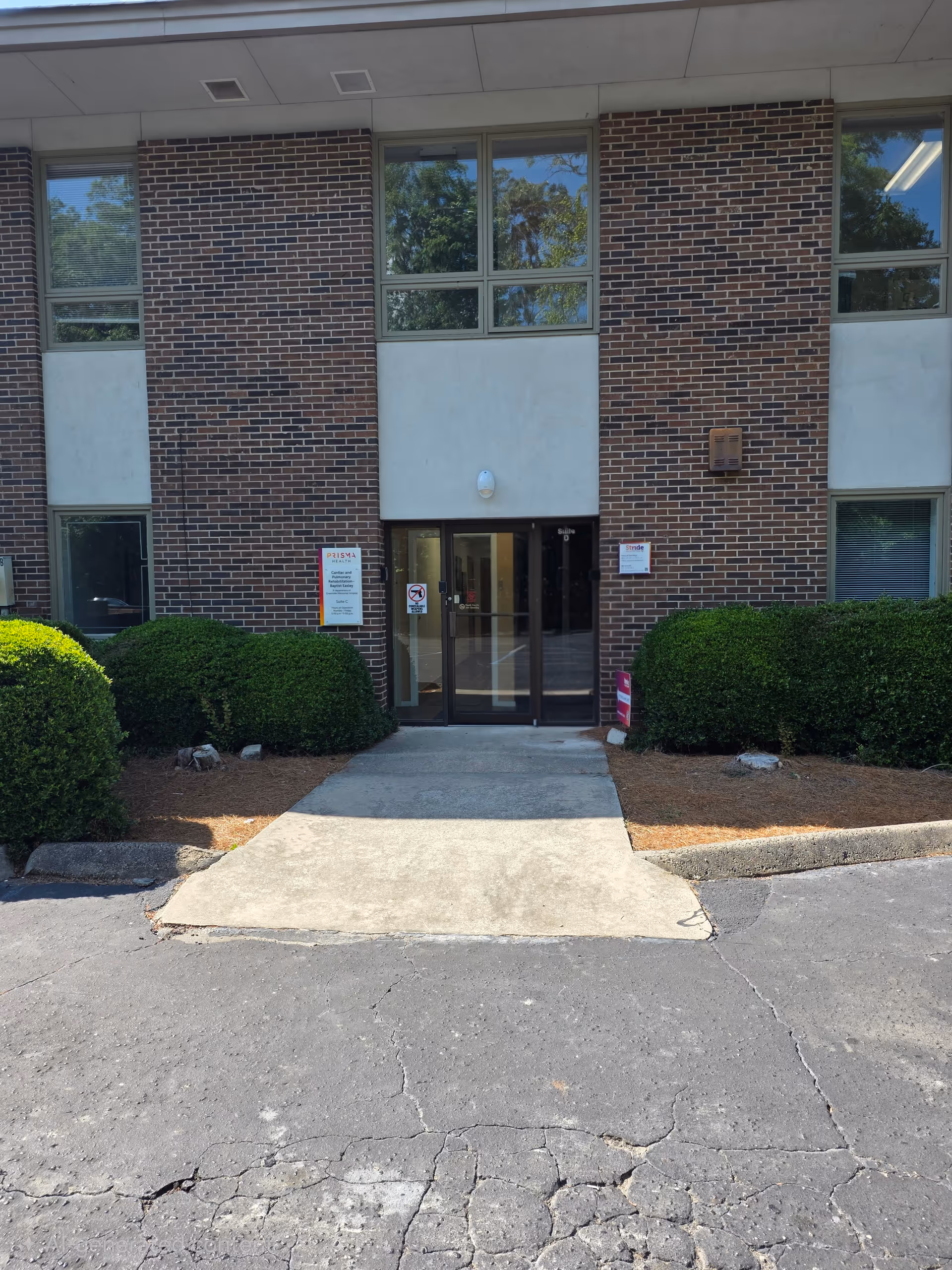 Brick senior living facility entrance with glass doors and manicured hedges on both sides.