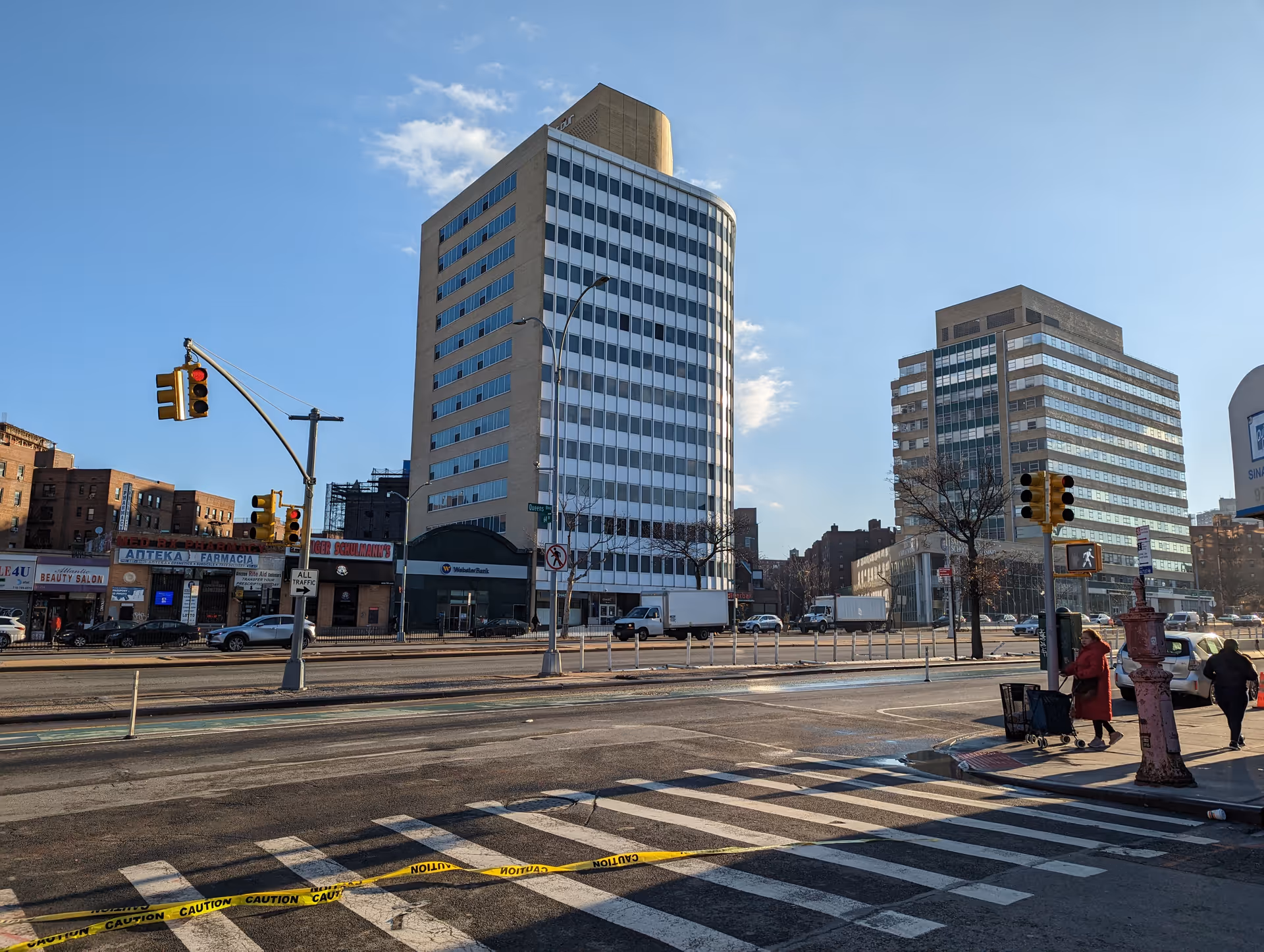 Exterior city street scene with tall office buildings, crosswalk, traffic lights, and pedestrians.