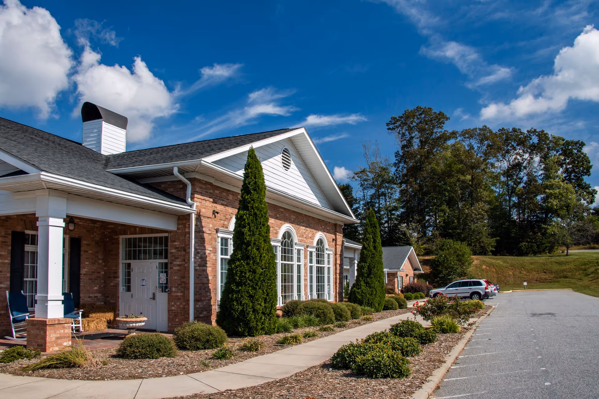 Brick assisted living building with arched windows, entrance porch, and parking lot.