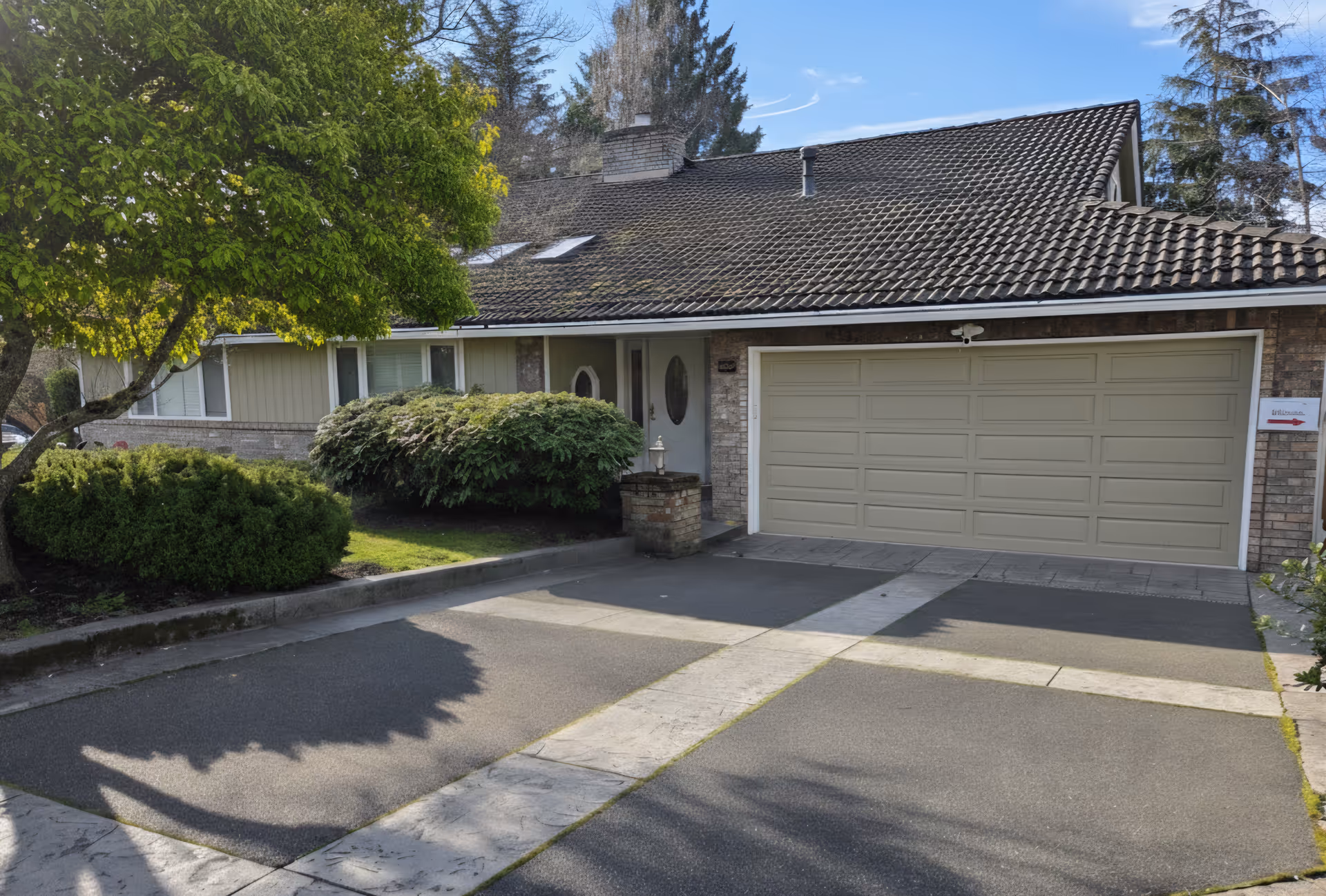 Residential house with a beige two-car garage, driveway, and manicured front yard.