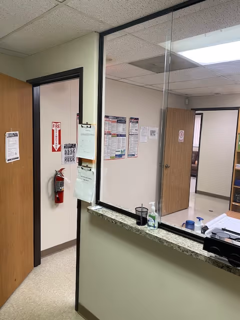 Interior hallway of a facility with a counter, glass window, and bulletin boards.