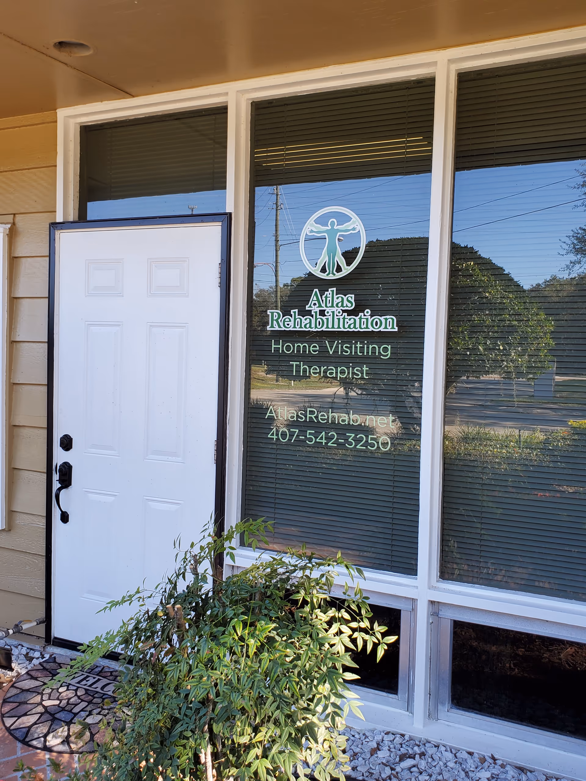 Front entrance of Atlas Rehabilitation with door, glass window sign, and surrounding plants.