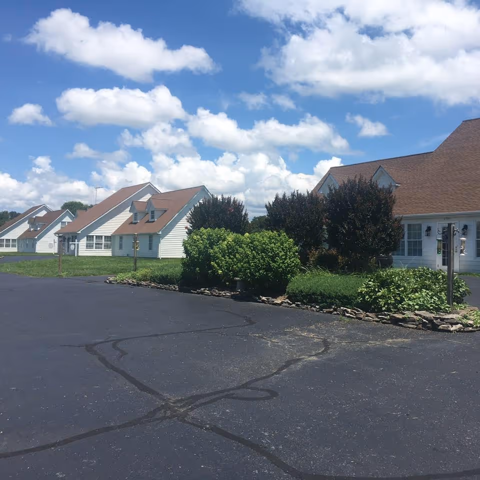 Front view of Taylor Farm Assisted Living Aaron House with white cottages and landscaping.