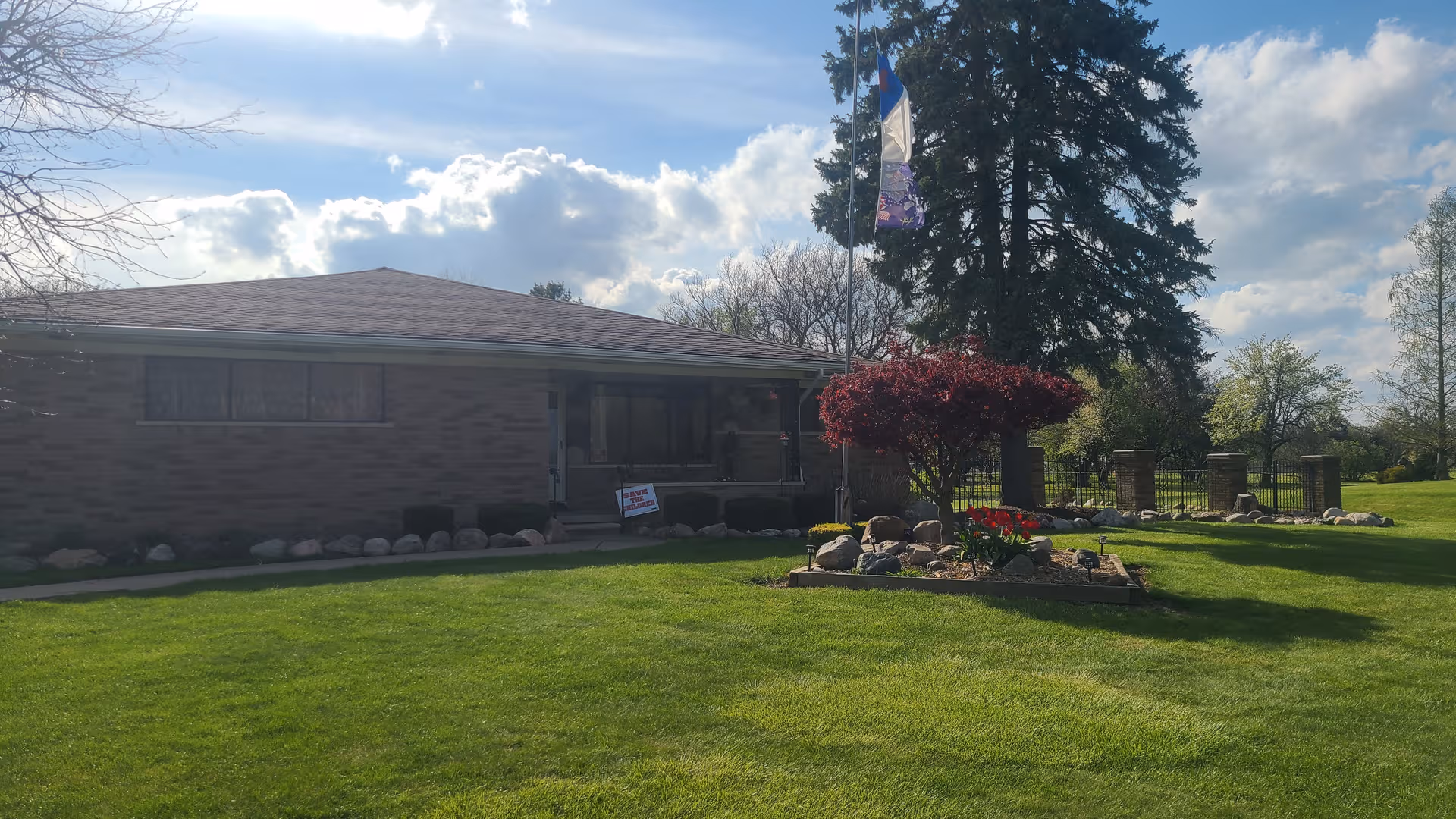 Single-story brick senior facility with a manicured lawn and landscaped flower bed in front.