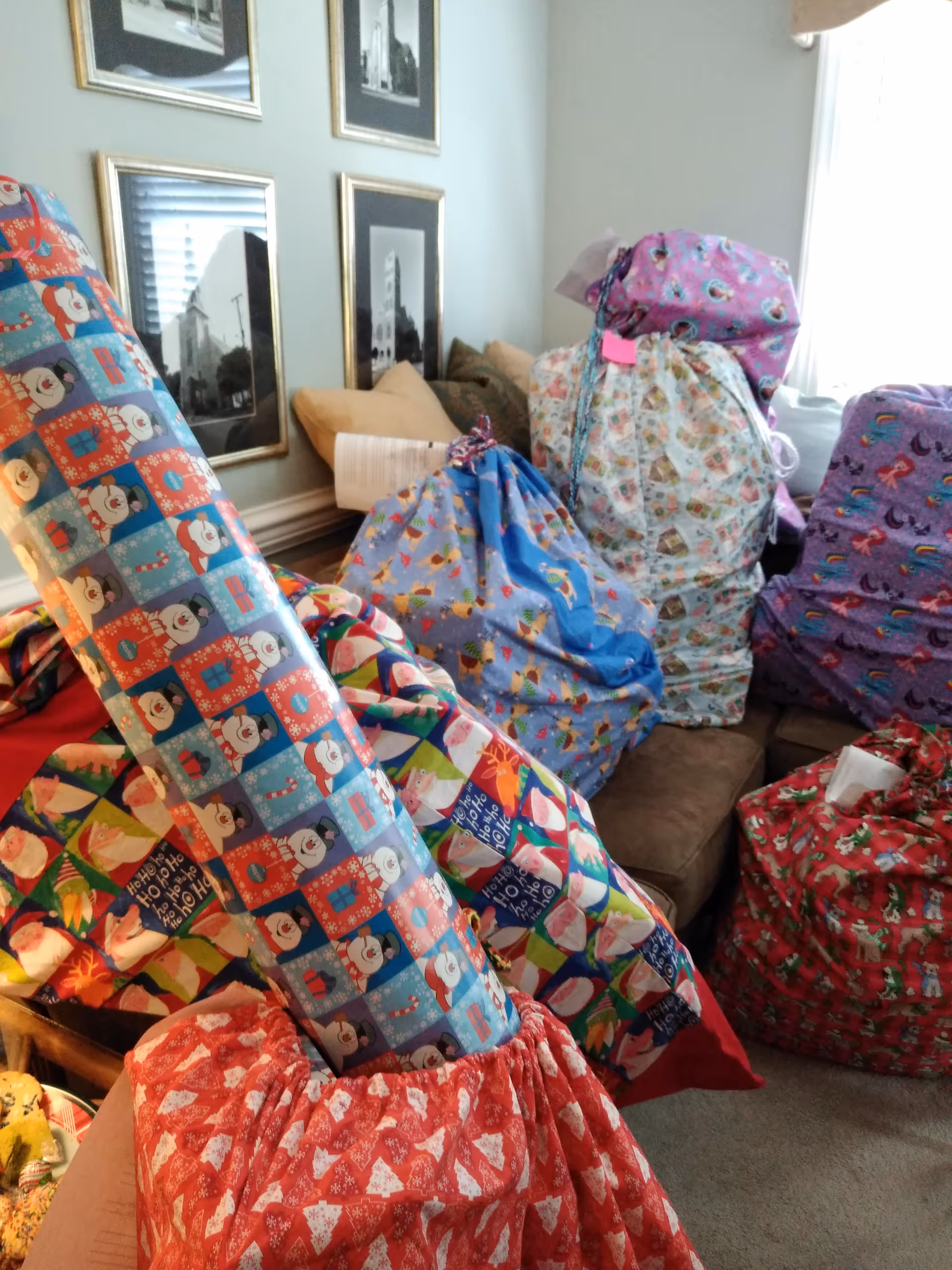 A cluttered living room corner filled with colorful wrapped gifts and patterned fabric bags.